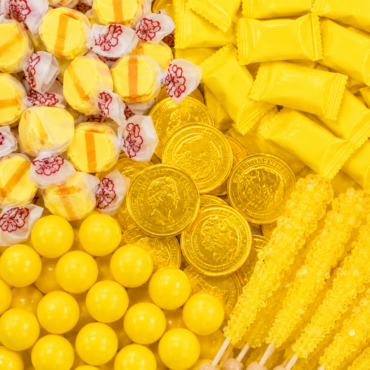 Yellow candy assortment featuring striped taffy, yellow wrapped candies, chocolate coins, gumballs, and rock candy sticks.