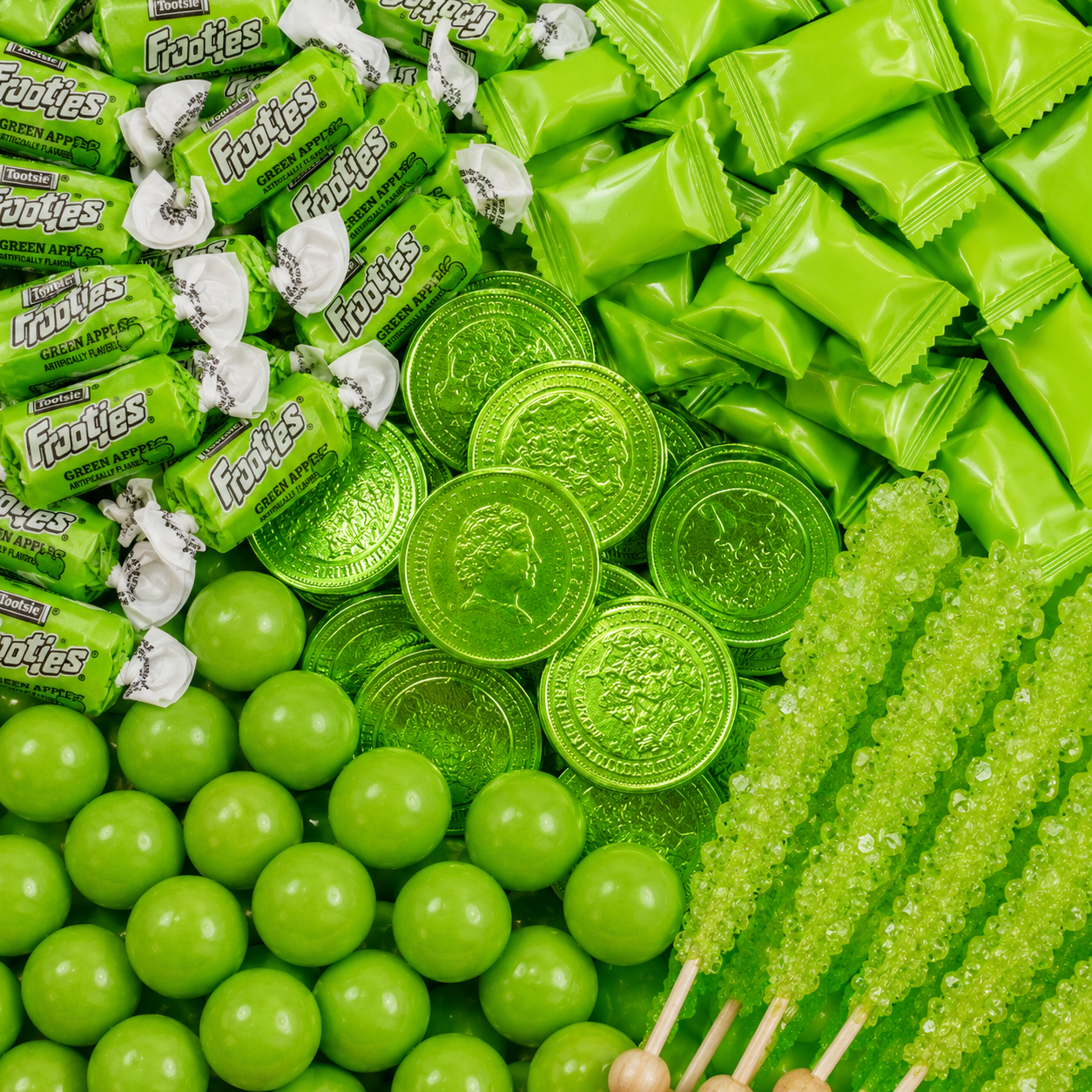 Green candy assortment featuring green apple Tootsie Frooties, green wrapped candies, chocolate coins, gumballs, and rock candy sticks.
