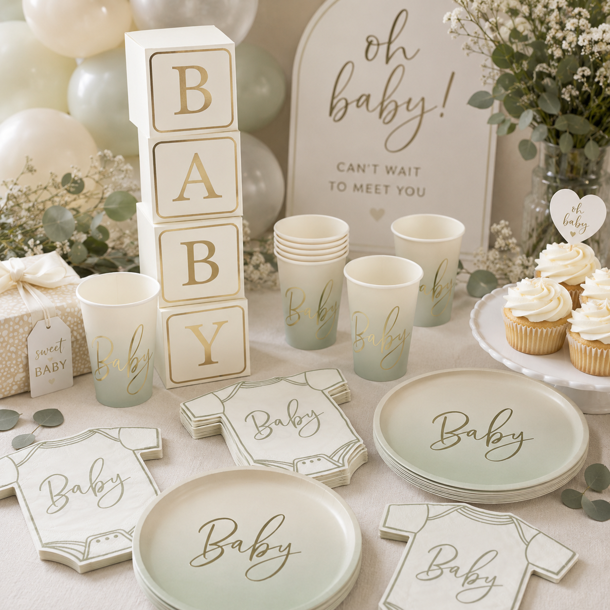 Neutral baby shower table setup featuring cream and sage green “Baby” plates, cups, and onesie napkins, stacked baby block decorations, an “Oh Baby!” sign, soft balloons, eucalyptus greenery, cupcakes, and white and gold accents.