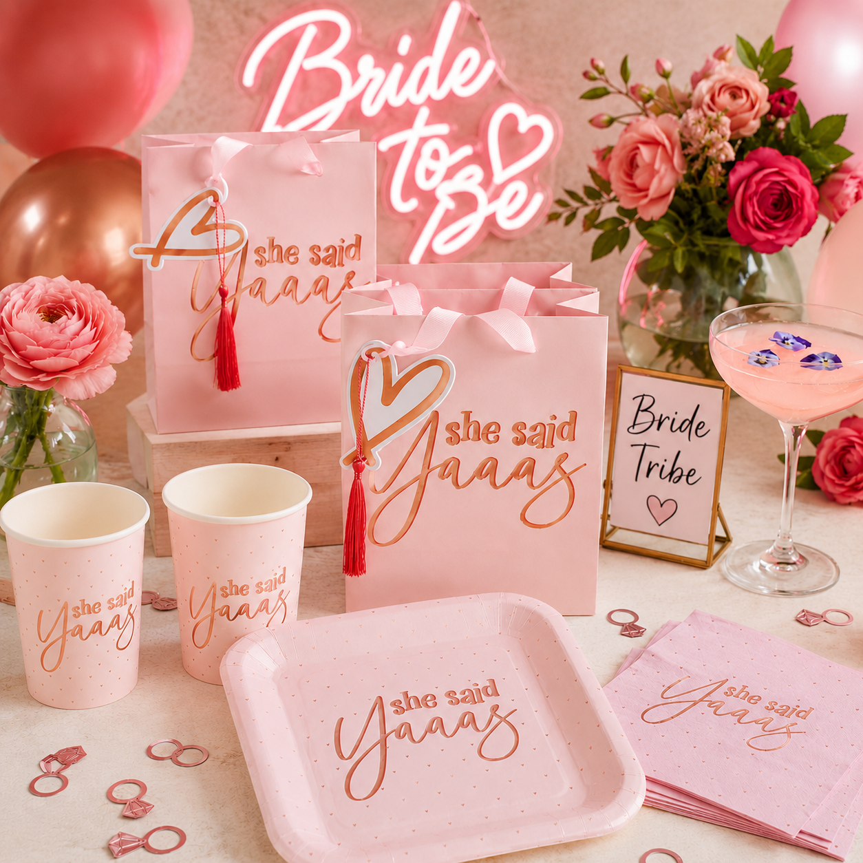 Pink bachelorette party setup with “She Said Yaaas” favor bags, matching cups, plate and napkins, neon sign, balloons, roses, cocktail, ring confetti, and pink bridal decor.