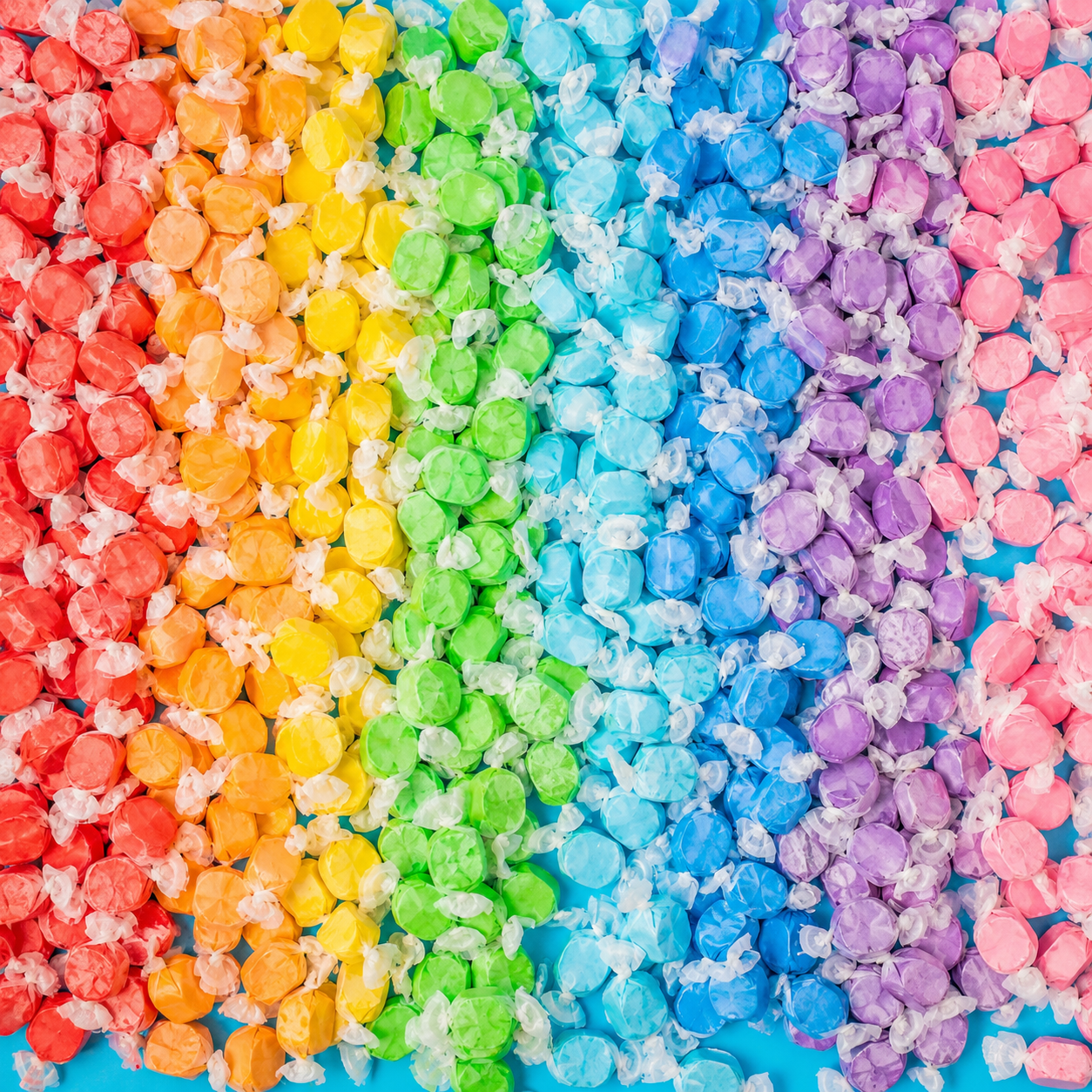 Rainbow rows of individually wrapped salt water taffy in red, orange, yellow, green, blue, purple, and pink arranged on a bright blue background.