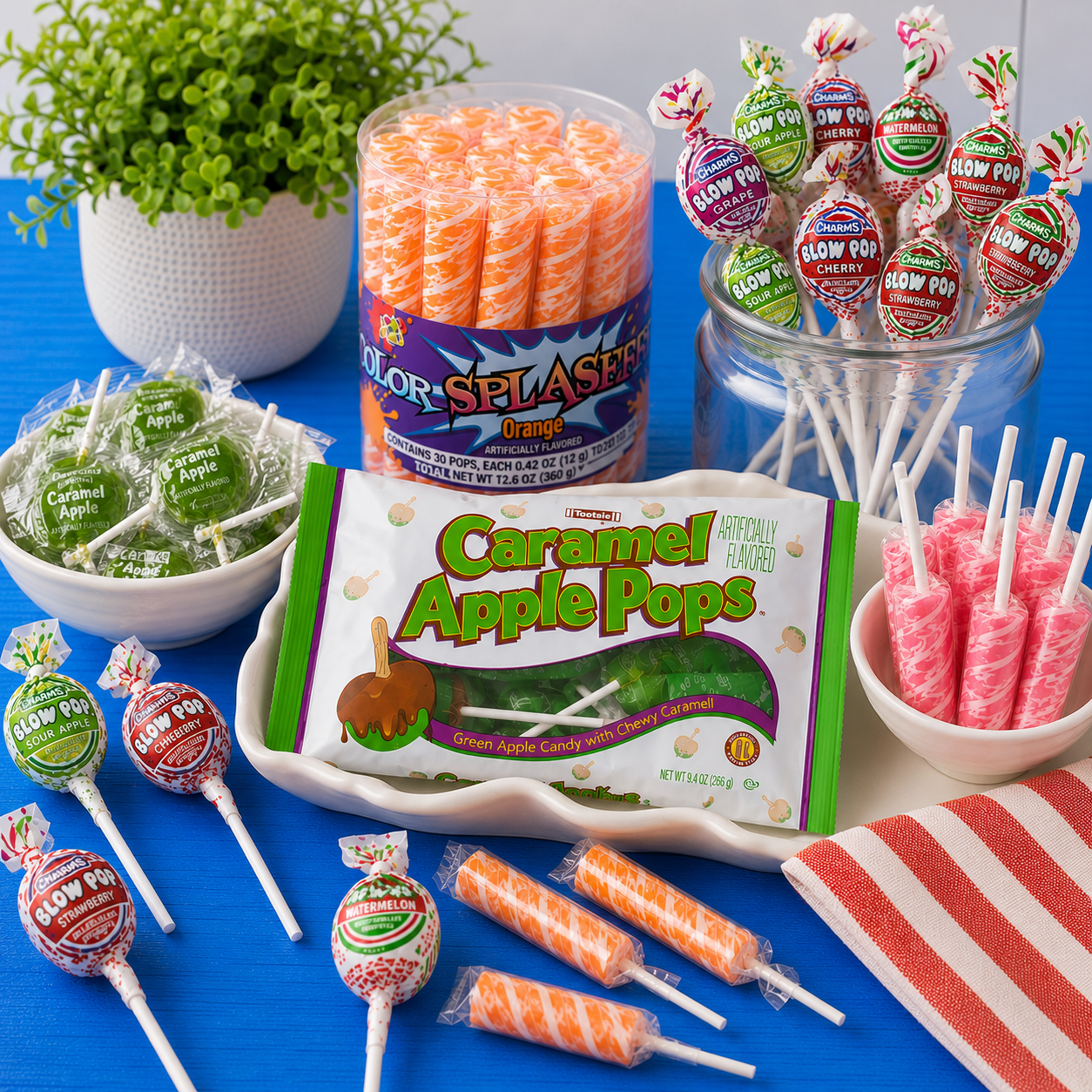 Assorted lollipops and suckers displayed on a bright blue table, featuring Caramel Apple Pops, colorful Blow Pops, orange swirl lollipops, and pink cylinder-shaped suckers in bowls and jars.