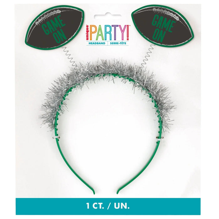 Green headband with silver tinsel pom-poms on top and two black foam football-shaped attachments reading "Game On" in green text.