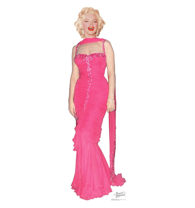 Vintage-style cardboard standup cutout of a woman with platinum blonde curled hair wearing a form-fitting hot pink sequined gown with a sheer neckline and trailing scarf against a white background.