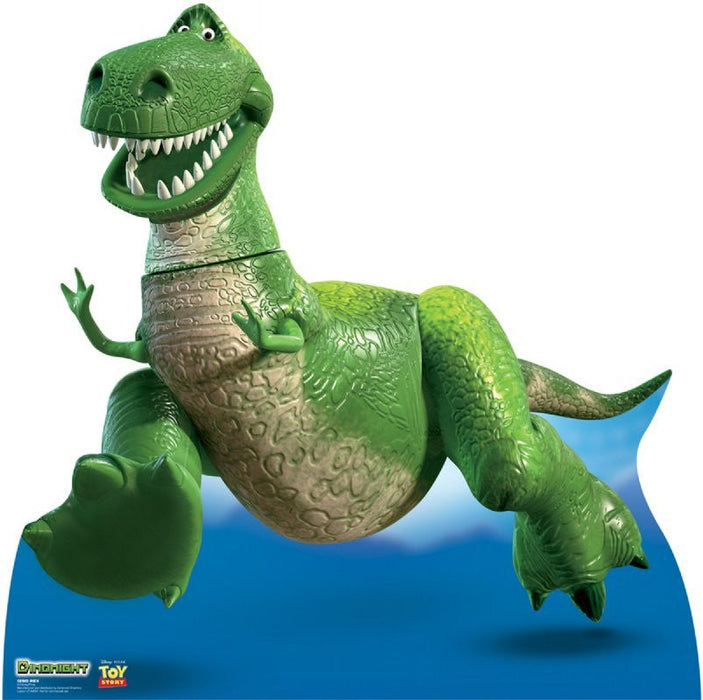 Green dinosaur character with wide grinning teeth, tan belly scales, and a blue fin tail, posed against a blue background on a cardboard standup.