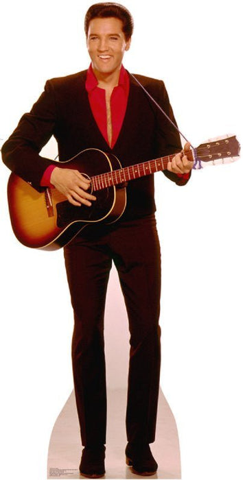 Cardboard standup cutout of a man in a brown velvet suit and red shirt holding a sunburst acoustic guitar, life-size figure with reddish-brown hair smiling at the camera.