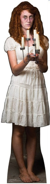 Woman with long curly reddish-brown hair wearing a cream-colored tiered dress, holding a cross and candle, displayed as a life-size cardboard standup figure.