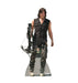 Life-size cardboard standup of a man with shoulder-length dark hair wearing a black sleeveless vest and distressed pants, holding a compound crossbow with green-fletched arrows.