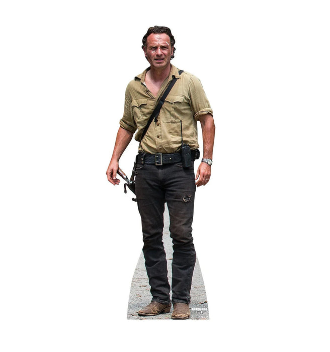 Lifesize cardboard standup figure of a man wearing a tan short-sleeved shirt, dark jeans with a studded belt, and brown boots, holding a revolver at his side.