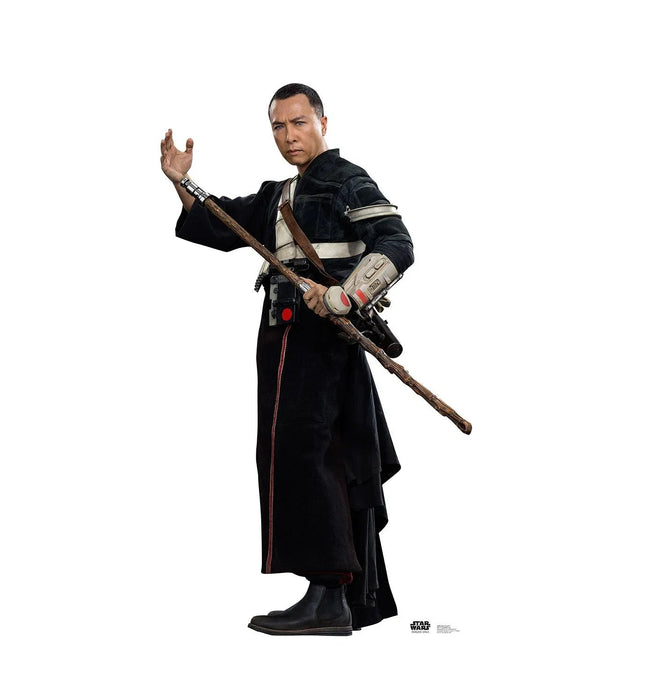 Man in black robes with white arm guard holding wooden staff with attached blaster, hand raised, against white background.