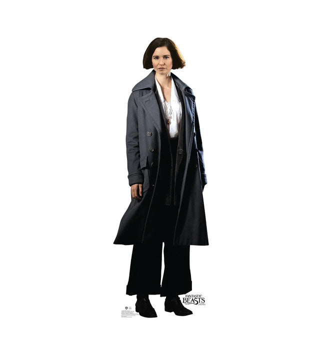 Woman with short dark hair wearing a long dark coat over a white blouse and black pants, standing against a white background.