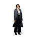 Woman with short dark hair wearing a long dark coat over a white blouse and black pants, standing against a white background.