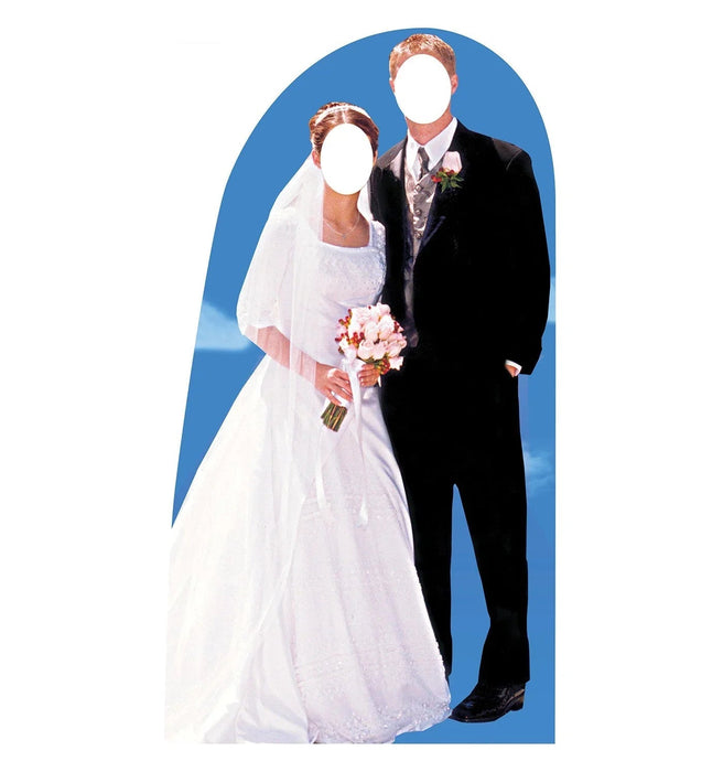 Life-size cardboard cutout of a bride in a white lace wedding dress holding a bouquet and a groom in a black tuxedo with boutonniere, both with blank white faces, set against a blue arched background.