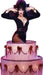 Lifesize cardboard standup of Elvira emerging from a two-tiered pink cake decorated with red bows, wearing a black low-cut outfit with purple hair and dramatic makeup.