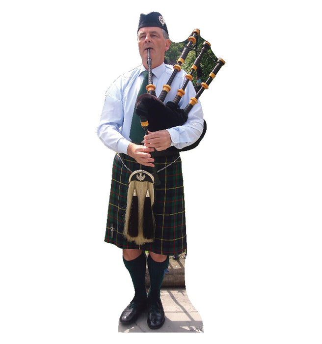 Man in traditional Scottish tartan kilt and white shirt playing bagpipes, wearing a dark blue cap, displayed as a full-size cardboard standup cutout.
