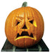 Carved jack-o'-lantern pumpkin with illuminated triangular eyes, nose, and frowning mouth, mounted on a black platform base.
