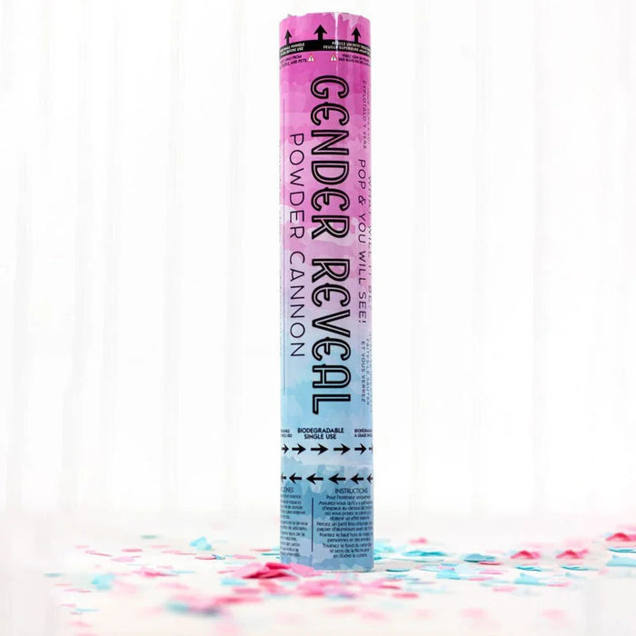 Pink and blue ombre cylindrical powder cannon with "Gender Reveal Powder Cannon" text, surrounded by scattered pink and blue confetti pieces on a white surface.