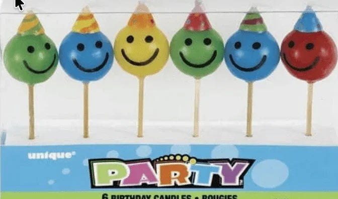 Six colorful smiley face candles on sticks in green, blue, yellow, green, blue, and red with party hats on top, displayed in packaging labeled "Party" with "6 Birthday Candles" text.