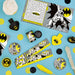 Batman favor pack assortment with themed activity sheets, rulers, discs, whistles, and black and yellow superhero party favors on a blue table.