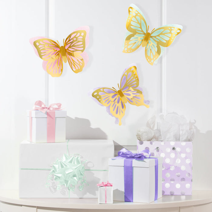 Butterfly Shimmer cutout wall butterflies in pastel pink, teal, and purple with metallic gold wing details displayed above wrapped gifts.