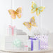 Butterfly Shimmer cutout wall butterflies in pastel pink, teal, and purple with metallic gold wing details displayed above wrapped gifts.