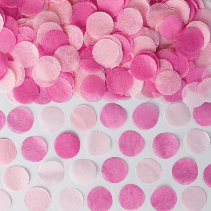 Pink tissue confetti circles in varying shades of pink arranged on a white surface for gender reveal party decoration.
