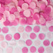 Pink tissue confetti circles in varying shades of pink arranged on a white surface for gender reveal party decoration.
