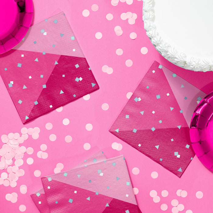 Turning Pink luncheon napkins in layered pink geometric confetti design, styled on a pink party table with matching plates, cups, and scattered confetti, 16-count pack.
