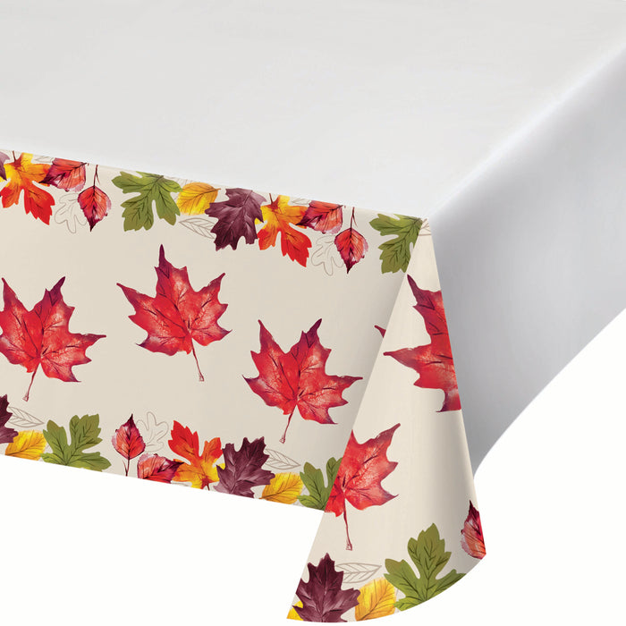 A tablecloth with a repeating pattern of red, orange, yellow, and green autumn maple leaves on a warm cream background, draped over a white surface.