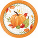 A round paper plate with an autumn harvest design, featuring a large orange pumpkin, a green gourd, a red apple, and orange and red leaves on a white plaid background with a bright orange rim.