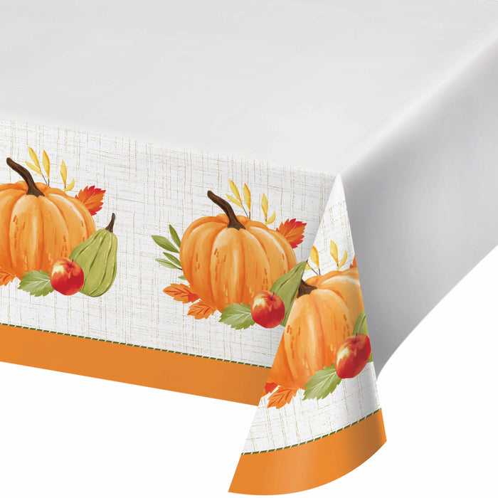 A white tablecloth with an autumn harvest pattern featuring orange pumpkins, green pears, red apples, and fall leaves, finished with a solid orange border.
