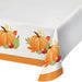 A white tablecloth with an autumn harvest pattern featuring orange pumpkins, green pears, red apples, and fall leaves, finished with a solid orange border.