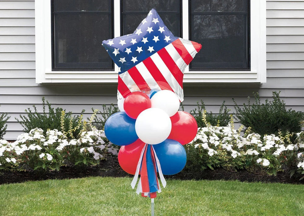 Patriotic yard sign featuring a large star-shaped balloon with white stars on blue and red and white stripes, topped with red, white, and blue balloons arranged below and ribbon streamers.