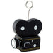 Black decorative camera-shaped balloon holder with white circular eyes, gold trim, a lens detail on the front, and a wire loop on top for hanging.