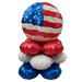 Stack of four metallic balloons in patriotic colors: an American flag-patterned sphere on top, red boxing gloves, white cloud shape, and blue fist at the base.