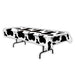 Black and white cow print plastic tablecloth with metal folding legs, measuring 54 by 108 inches.