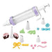 Cake decorating kit with a clear syringe-style dispenser with purple bands and white plunger, shown with eight white piping tips and colorful icing decorations including pink frosting, yellow bow, blue swirls, and green shapes.