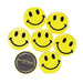Seven bright yellow smiley face pins with black eyes and smiles arranged in a circle, plus one shown from the back displaying its metal pin fastener.