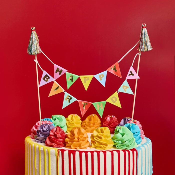 Colorful birthday cake with rainbow frosting and a 'Happy Birthday' banner against a red background