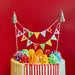 Colorful birthday cake with rainbow frosting and a 'Happy Birthday' banner against a red background
