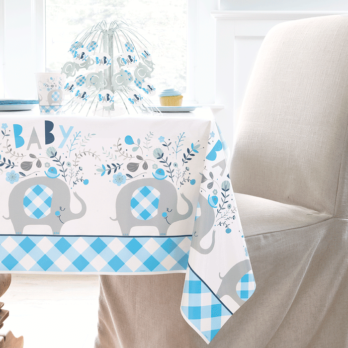 Blue floral elephant baby shower plastic tablecover with gray elephants, blue gingham accents, flowers, and “Baby” lettering on a party table.