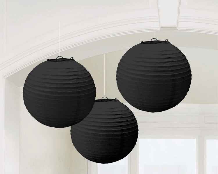 Three black paper lanterns with textured ribbed surfaces and hanging loops suspended against a white ceiling in an interior space.