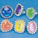 Six colorful gemstone rings with large faceted stones in blue, purple, green, orange, yellow, and pink, each surrounded by a band of rhinestones.