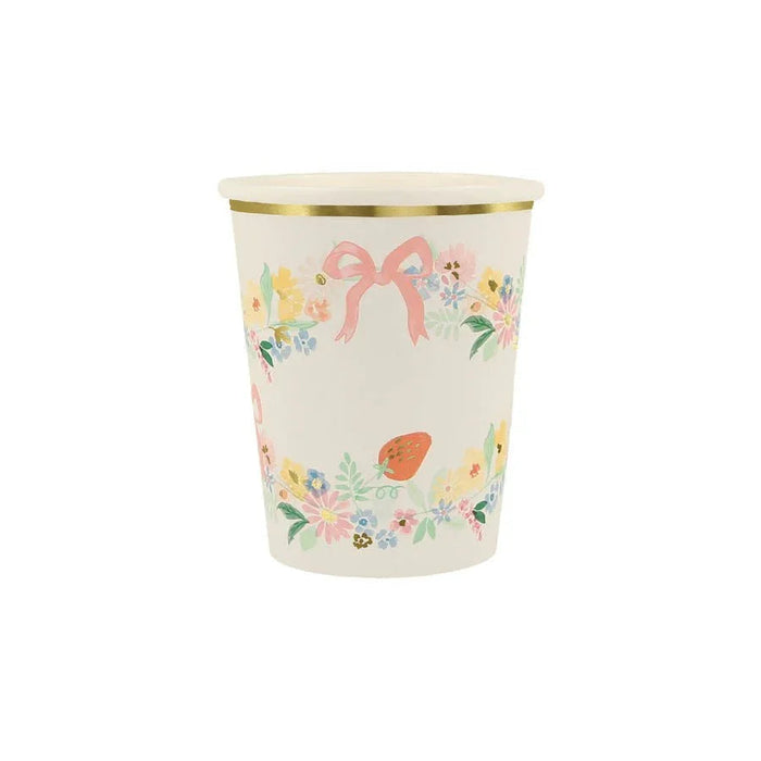Cream-colored paper cup with gold rim featuring watercolor floral garland, pink bow, and strawberry illustrations around the sides.