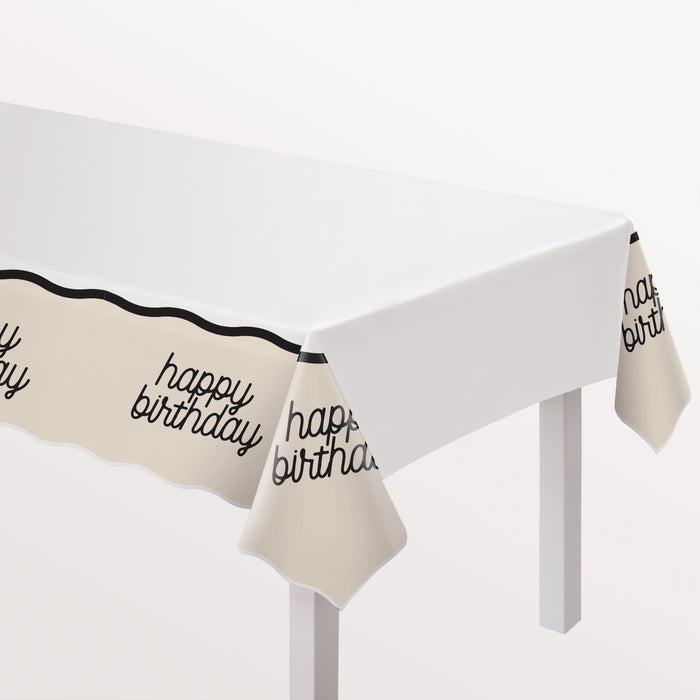 Birthday Chic Plastic Table Cover with a white top, cream draped border, black trim, and script happy birthday details.