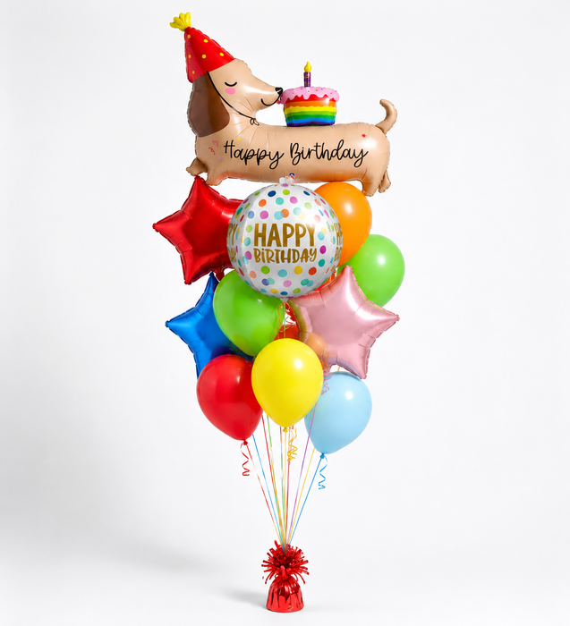 A birthday balloon bouquet featuring a dachshund-shaped foil balloon with a birthday cake and 'Happy Birthday' script, surrounded by assorted colorful balloons including red, orange, green, blue, yellow, pink, and light blue, with a red tassel at the base.