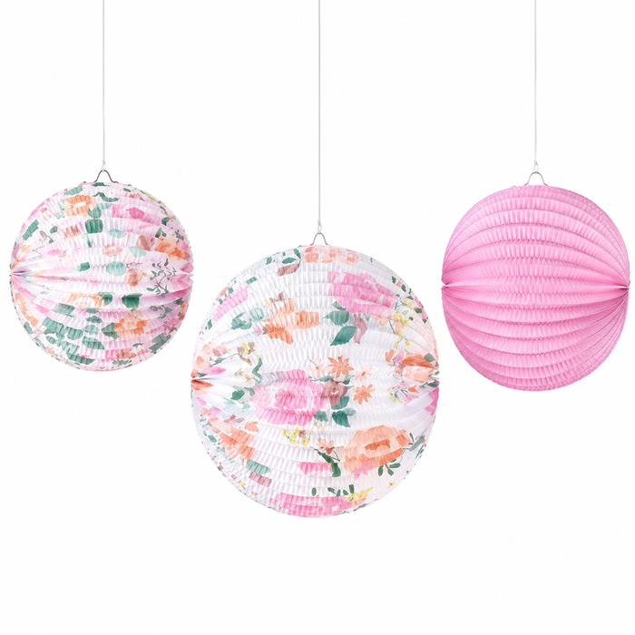 Floral paper lantern set with two round floral print lanterns and one solid pink lantern hanging on white strings.