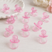 Several small pink crystal plastic pacifier favors scattered on a white tabletop, showing their translucent glossy finish from different angles.