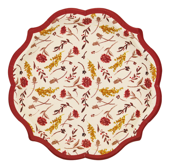A scalloped round paper plate with a cream background, featuring a dense floral and botanical pattern in red, mustard yellow, and brown, finished with a solid dark red border.