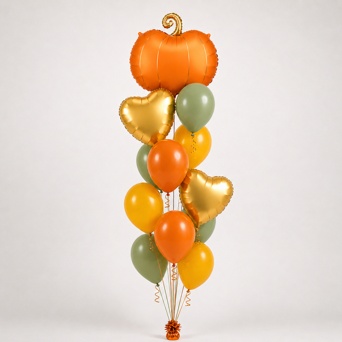 A vertical cluster of decorative balloons on a light gray studio background, including one large orange pumpkin-shaped balloon, several metallic gold heart-shaped balloons, orange and yellow latex balloons, and muted sage green latex balloons.